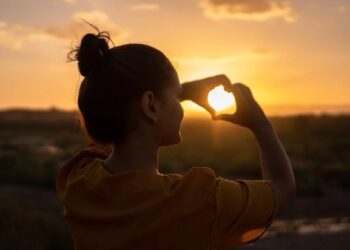 Chica formando corazon con las manos en atardecer